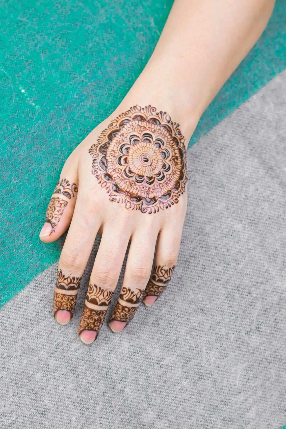 Hands held out to show fresh mehndi against a bright dupatta